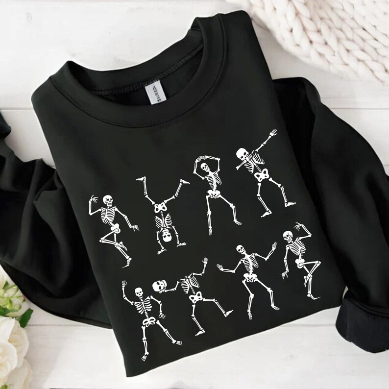 K&ouml;nnte beinhalten: Schwarzes Sweatshirt mit Rundhalsausschnitt und wei&szlig;em Skelett-Design. Das Design zeigt mehrere Skelette in verschiedenen Tanzposen. Das Sweatshirt ist aus weichem Material und ideal f&uuml;r Halloween.