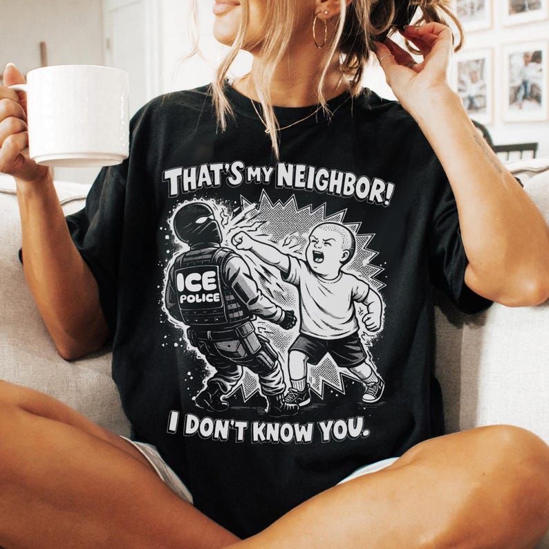 K&ouml;nnte beinhalten: Schwarzes T-Shirt mit einer grafischen Illustration. Die Illustration zeigt ein Kind, das einen ICE-Polizisten schl&auml;gt. Der Text auf dem Shirt lautet: "THAT'S MY NEIGHBOR! I DON'T KNOW YOU."