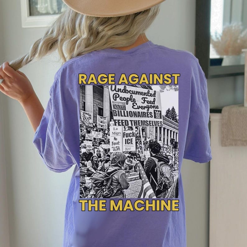 Puede incluir: Camiseta de color lila claro con un gr&aacute;fico en la espalda. El gr&aacute;fico en blanco y negro muestra una protesta con el texto "RAGE AGAINST THE MACHINE". El texto dice "Undocumented People Feed Everyone Billionaires Feed Themselves".
