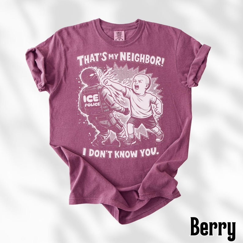 K&ouml;nnte beinhalten: Beerenfarbenes T-Shirt mit einer grafischen Illustration. Die Illustration zeigt ein Kind, das einen ICE-Polizisten schl&auml;gt, mit dem Text "THAT'S MY NEIGHBOR! I DON'T KNOW YOU." ober- und unterhalb des Bildes.
