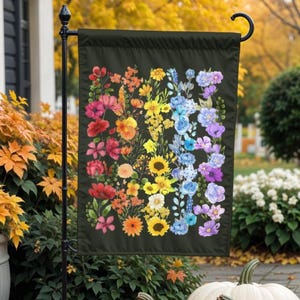 May include: A garden flag with a black background and a rainbow of colorful flowers. The flowers are arranged in a vertical line, with the red flowers at the top and the purple flowers at the bottom.