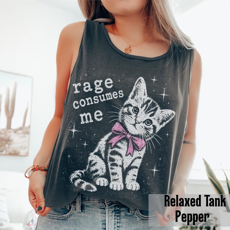 May include: A charcoal gray sleeveless tank top featuring a white graphic of a tabby kitten wearing a pink bow. The text "rage consumes me" is printed in white above the kitten, surrounded by small white star accents on the front of the shirt.