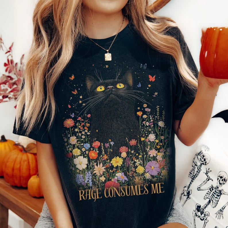 May include: Black t-shirt with a black cat surrounded by colorful flowers. The text "RAGE CONSUMES ME" is printed on the bottom of the shirt.