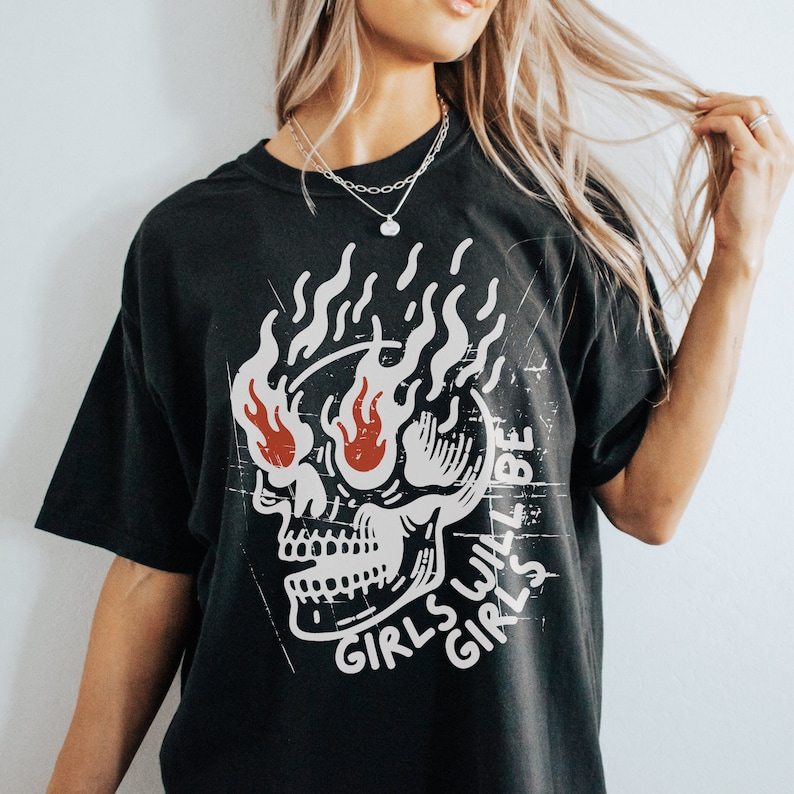 May include: Black t-shirt featuring a graphic of a skull with flames and the text "Girls will be girls" in white.