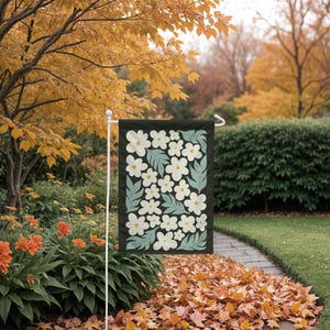 May include: A black garden flag with a white floral pattern. The flowers are stylized and have a yellow center. The background is a dark green color.