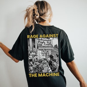 May include: Black t-shirt with a graphic that reads "RAGE AGAINST THE MACHINE." The graphic includes the text "Undocumented People Feed Everyone Billionaires Feed Themselves" over a black and white image of a protest.