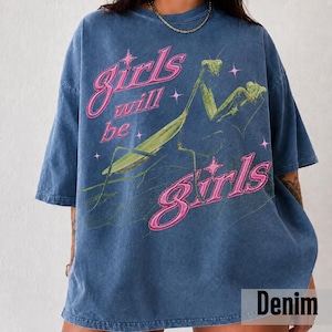 以下が含まれることがあります： 緑色のカマキリのグラフィックと、小さな星に囲まれたピンク色の「girls will be girls」という文字がプリントされた、ブルーのケミカルウォッシュ加工Tシャツ。半袖でクルーネックの、ゆったりとしたリラックスフィットのデザイン。