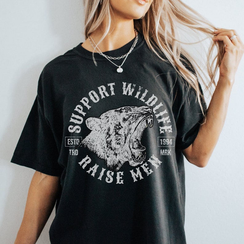 May include: Black t-shirt with a white graphic of a roaring tiger head inside a circle with the text "Support Wildlife" above the tiger and "Raise Men" below the tiger. The text "Estd 1994" is on the right side of the circle.