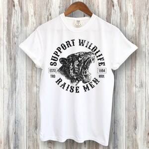 May include: White t-shirt with a black graphic print of a roaring tiger head in a circle. The text "Support Wildlife Raise Men" is printed around the tiger head. The text "Estd. 1994 Trd. Mrk." is printed below the tiger head.