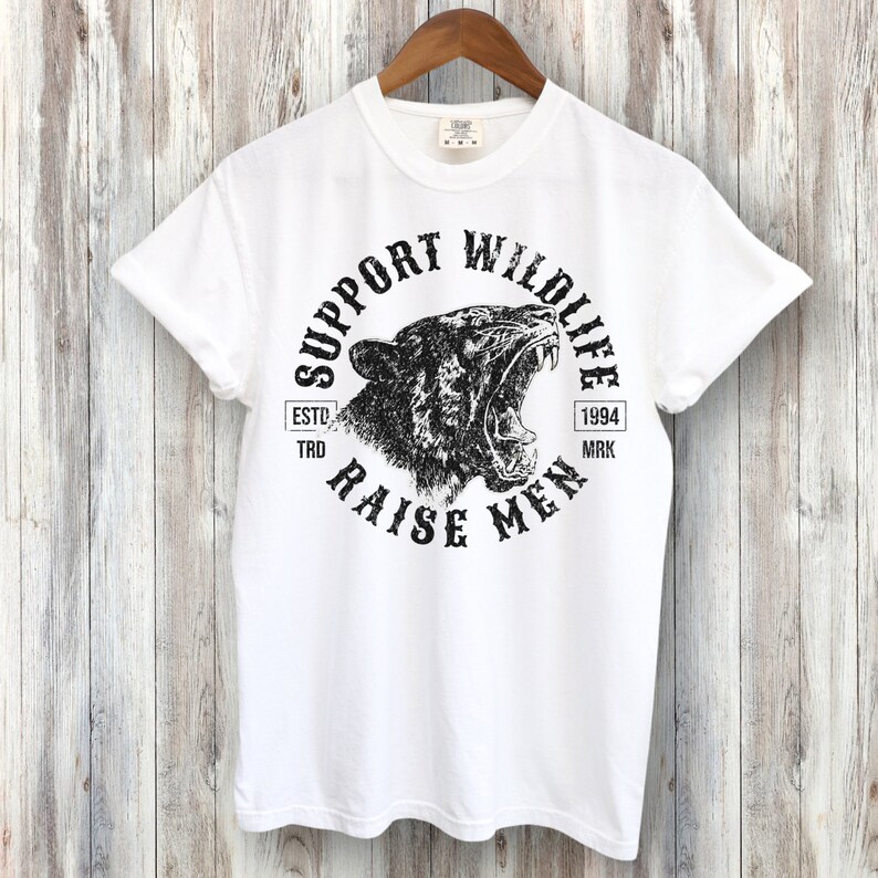 May include: White t-shirt with a black graphic print of a roaring tiger head in a circle. The text "Support Wildlife Raise Men" is printed around the tiger head. The text "Estd. 1994 Trd. Mrk." is printed below the tiger head.