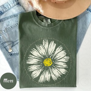 May include: A moss green t-shirt with a white daisy graphic and the text "You're braver than you think,  find the things that make you feel alive,  and then,  jump."