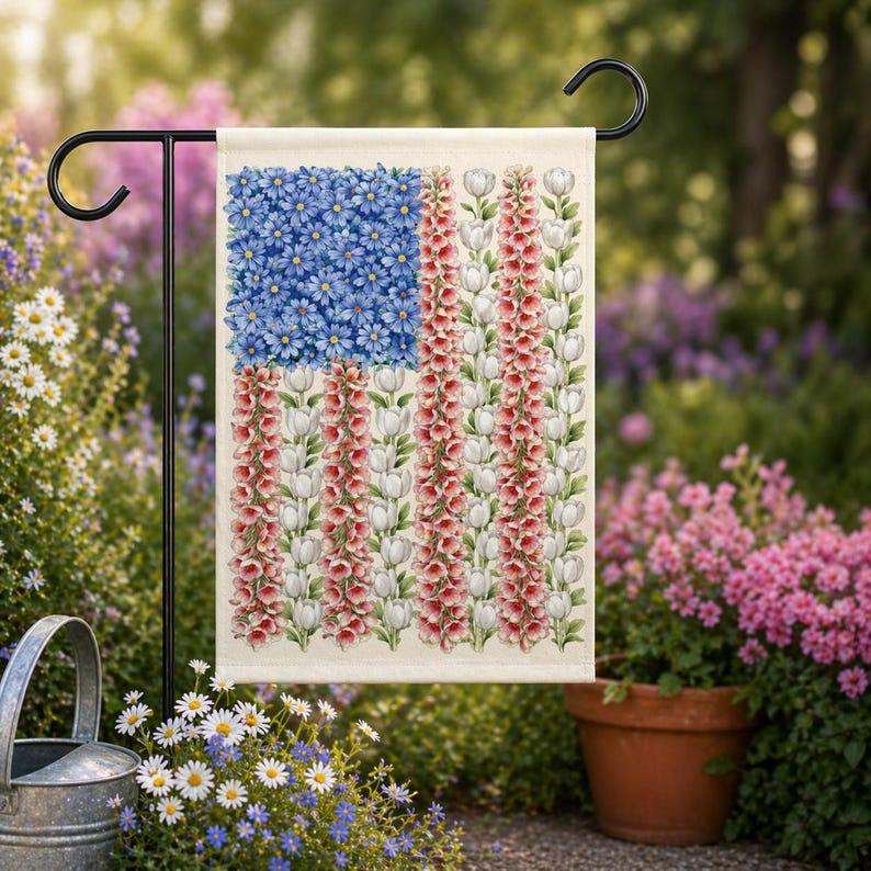 May include: A garden flag featuring a floral American flag design. The flag's blue field is composed of blue flowers, while the stripes are made of red and white flowers. The flag is displayed on a black metal stand in a garden setting.