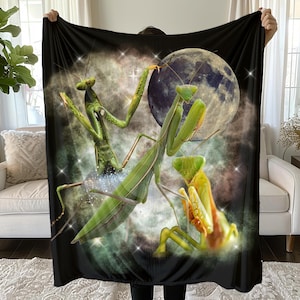 May include: Black blanket featuring a vibrant illustration of three praying mantises against a backdrop of a full moon and a starry nebula. The mantises are depicted in shades of green and yellow, with intricate details.