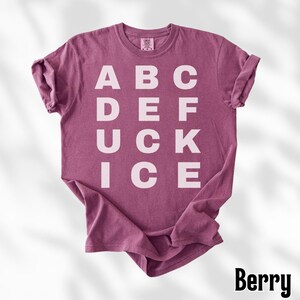 May include: Berry-colored t-shirt with the letters ABC, DEF, UCK, and ICE printed in white. The shirt has a crew neck and short sleeves. The word "Berry" is printed in a black, stylized font at the bottom right corner.