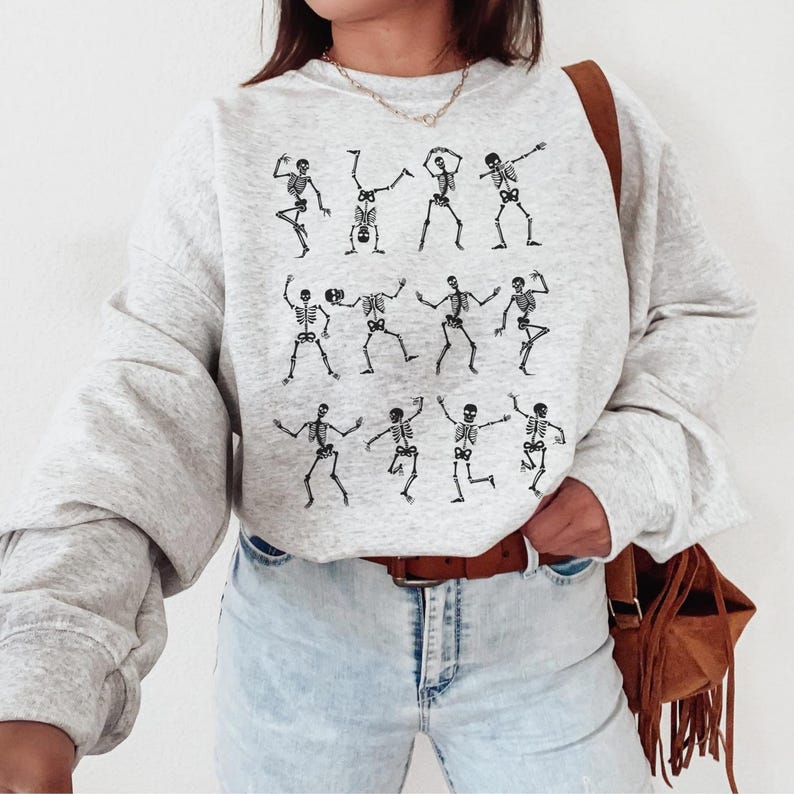 K&ouml;nnte beinhalten: Hellgraues Sweatshirt mit einer schwarzen Illustration tanzender Skelette. Die Skelette sind in verschiedenen Posen dargestellt. Das Sweatshirt hat lange &Auml;rmel und einen Rundhalsausschnitt.