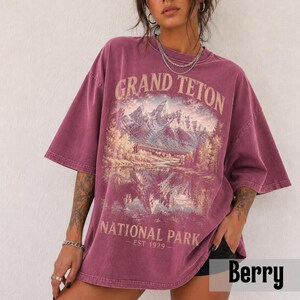 May include: Berry-colored oversized t-shirt featuring a scenic illustration of mountains and a lake, with the text "GRAND TETON NATIONAL PARK - EST 1979." The shirt has short sleeves and a relaxed fit, perfect for casual wear.