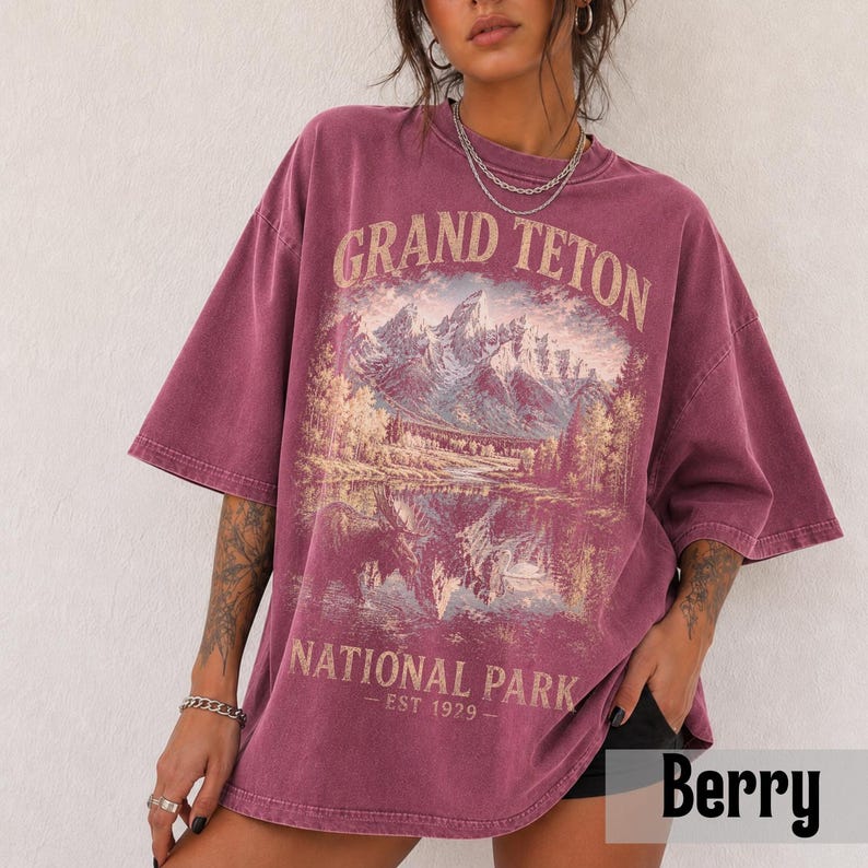 May include: Berry-colored oversized t-shirt featuring a scenic illustration of mountains and a lake, with the text "GRAND TETON NATIONAL PARK - EST 1979." The shirt has short sleeves and a relaxed fit, perfect for casual wear.