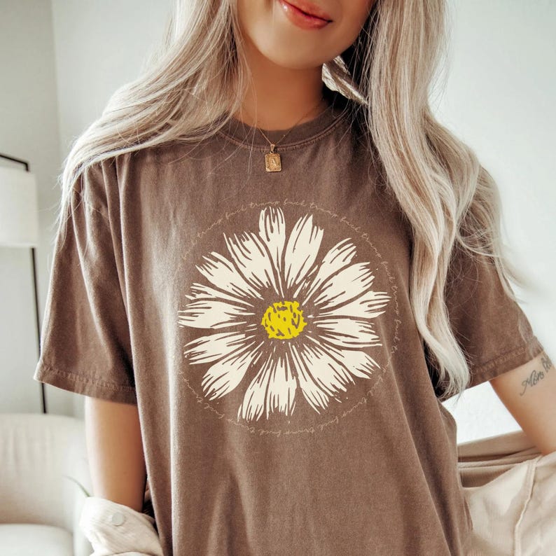 May include: Brown t-shirt with a white daisy graphic and the text "Find the good in the things you love, and love the things you find." printed around the flower.