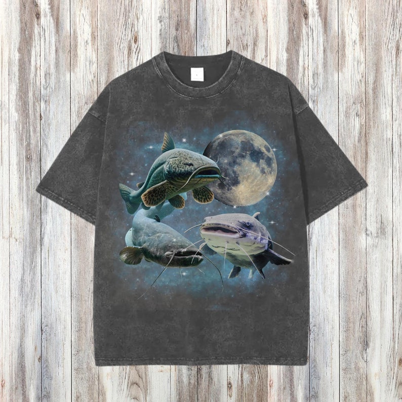 May include: A dark gray t-shirt with a graphic print of three catfish swimming in front of a full moon. The catfish are a light blue and gray color.