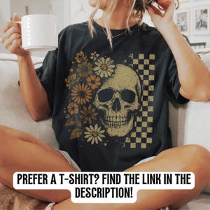 May include: Black t-shirt featuring a skull design with floral and checkered elements. The skull is surrounded by orange and yellow flowers. The text at the bottom of the image reads: PREFER A T-SHIRT? FIND THE LINK IN THE DESCRIPTION!