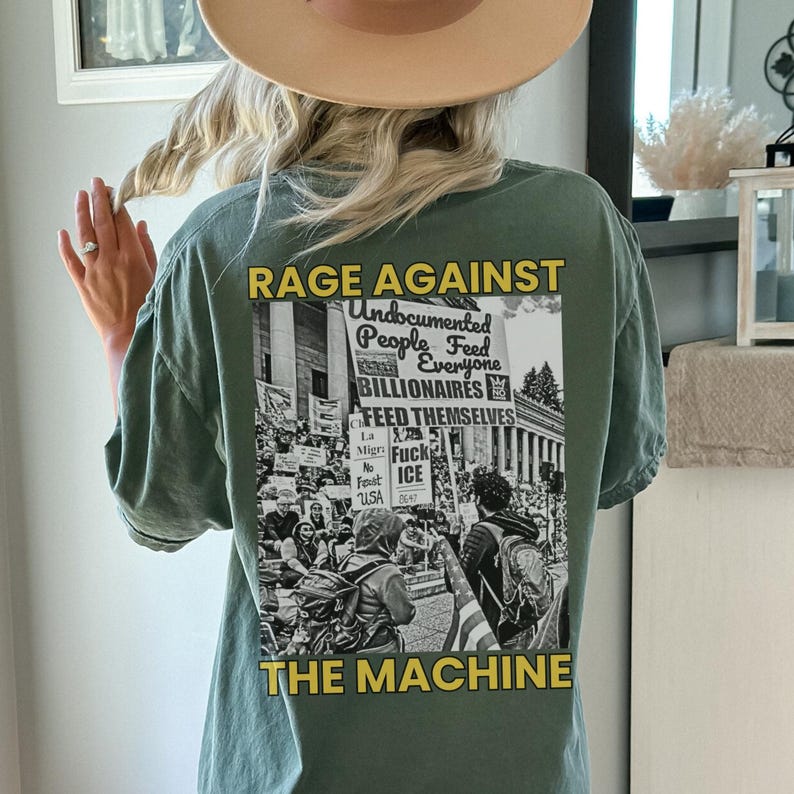 May include: Sage green t-shirt with a graphic on the back that reads "RAGE AGAINST THE MACHINE." The graphic includes text and a black and white image of a protest. The shirt is a casual, oversized fit.