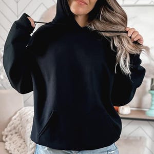 May include: A solid black hoodie with a front pocket and a drawstring hood. The hoodie is made of a soft material and is a casual style. The sleeves have ribbed cuffs. The hoodie is a versatile piece of clothing.