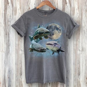 May include: A dark gray t-shirt with a graphic print of three catfish swimming in front of a full moon. The catfish are in shades of blue, green, and gray.