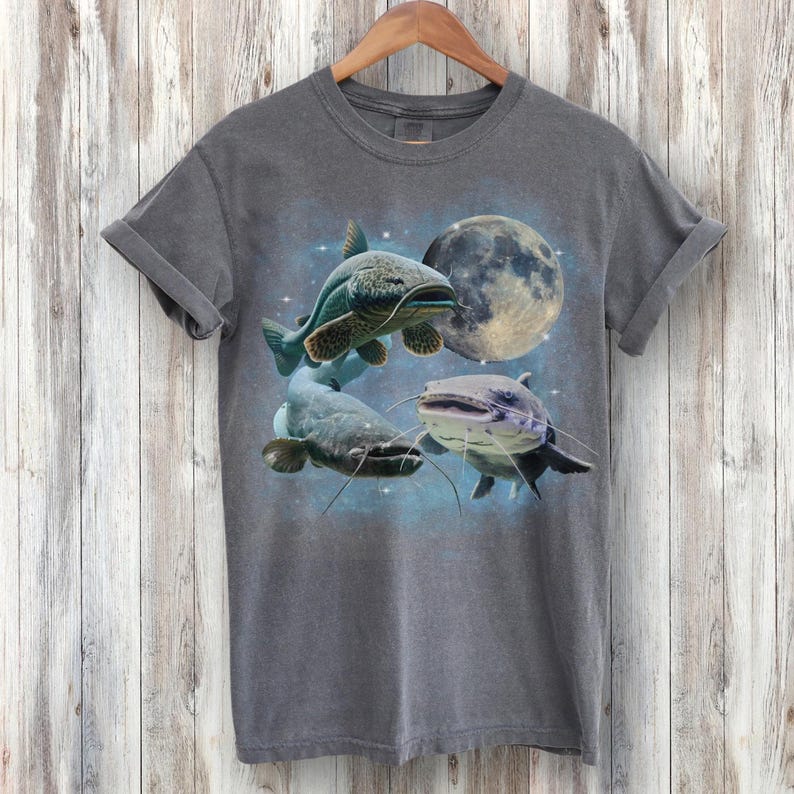 May include: A dark gray t-shirt with a graphic print of three catfish swimming in front of a full moon. The catfish are in shades of blue, green, and gray.