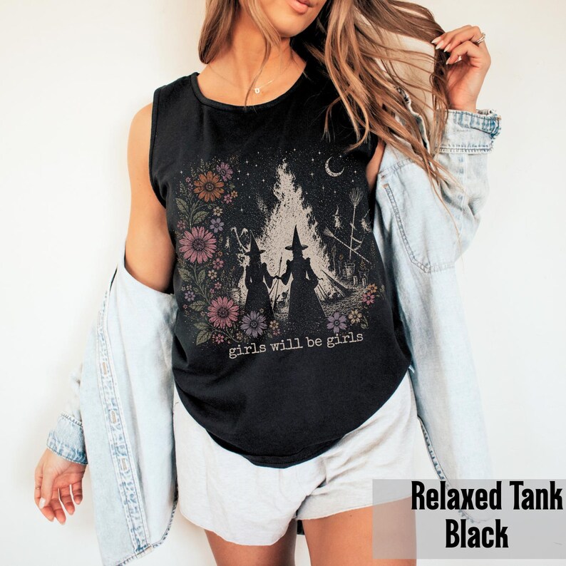 May include: Black relaxed tank top with a floral and witch graphic. The graphic features two witch silhouettes, flowers, and the text "girls will be girls". The tank top is sleeveless.