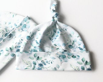 May include: A white baby hat with a knot on top. The hat has a blue and green watercolor floral pattern.