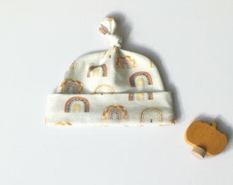 May include: A white baby hat with a knotted top and a pattern of colorful rainbows.
