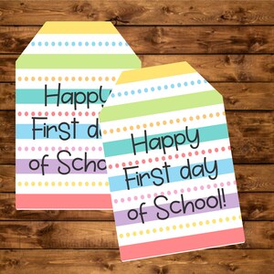 Puede incluir: Dos etiquetas de regalo coloridas con un diseño de rayas pastel y el texto "Happy First day of School!" en negro. Las etiquetas tienen una combinación de colores rosa claro, amarillo, verde, azul y morado con detalles de puntos.