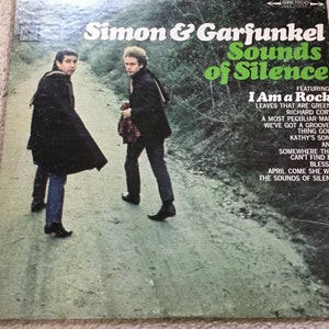 May include: Vintage vinyl record album cover for Simon & Garfunkel's "Sounds of Silence," featuring the duo walking on a path. The album title is in green, with song titles listed below, including "I Am a Rock."