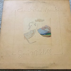 May include: A vintage vinyl record album cover with a light brown background. The album title "Court and Spark" is written in cursive script. A hand-drawn illustration of a cloud, mountains, and a field is in the center of the cover. The artist's name "Joni Mitchell" is written in cursive script at the bottom of the cover.