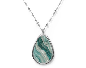May include: A silver necklace with a teardrop pendant. The pendant has a marbled design in teal, white, and grey, set within a silver frame. The chain is delicate. The pendant's pattern resembles flowing water.
