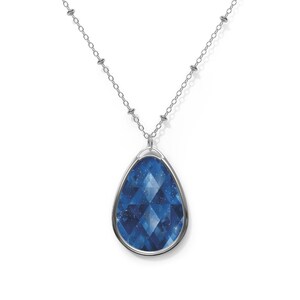 May include: A silver necklace with a teardrop-shaped pendant. The pendant features a faceted, deep blue gemstone with a starry pattern. The chain is delicate, with small, round beads interspersed along its length. The pendant is approximately 1.5 inches long.