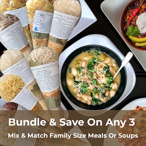 May include: An overhead shot showcases family-size meal kits and soups. Several cone-shaped packages of dried ingredients are visible, alongside bowls of prepared soup. The image includes text that reads "Bundle & Save On Any 3 Mix & Match Family Size Meals Or Soups."