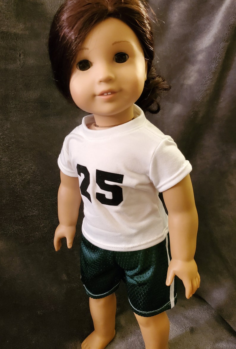 Pode incluir: Uma boneca vestindo uma camisa branca com o n&uacute;mero 25 na frente e shorts esportivos verdes com uma faixa branca na lateral.