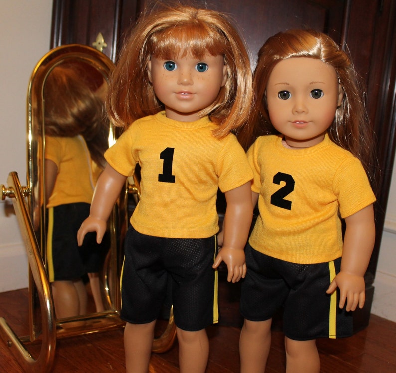 Pode incluir: Duas bonecas vestindo uniformes esportivos amarelos e pretos com os n&uacute;meros 1 e 2 na frente. As bonecas t&ecirc;m cabelo comprido, liso e ruivo e olhos azuis.