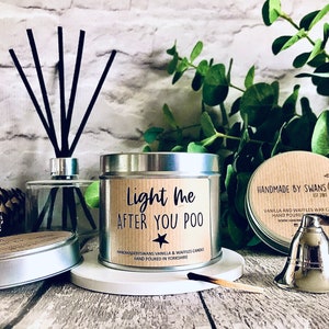 May include: A silver tin candle with a brown label that reads "Light me after you poo." The candle is surrounded by matches, a silver candle snuffer, and a diffuser.