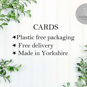 May include: White background with green leafy branches on either side. Text reads "CARDS" in black. Below the text are three bullet points with the following text: "Plastic free packaging", "Free delivery", and "Made in Yorkshire". The text "HANDMADE BY SWANS" is in a gray circle with a white outline and a white silhouette of a swan inside the circle.