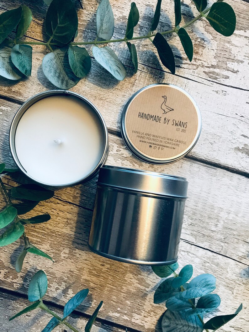 May include: A silver tin candle with a brown paper label that reads "Handmade by Swans Est 2015" and "Vanilla and Waffles Wax Candle Hand Poured in Yorkshire www.handmadebyswans.com".