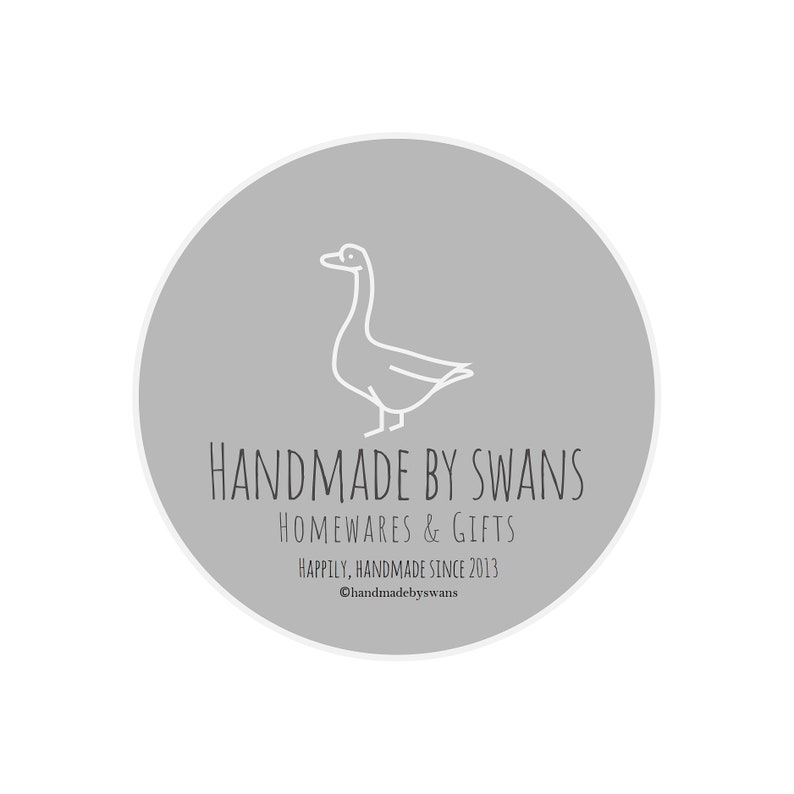 May include: A gray circle with a white outline, featuring a line drawing of a goose. The text "HANDMADE BY SWANS" is written in black below the goose, followed by "HOMEWARES & GIFTS" and "Happily, Handmade Since 2013". The text "@handmadebyswans" is written in black at the bottom of the circle.