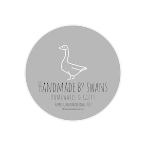 Puede incluir: Un logotipo circular con fondo gris claro y un dibujo lineal blanco de un cisne. El texto dice HANDMADE BY SWANS, HOMEWARES & GIFTS, HAPPILY, HANDMADE SINCE 2013 y @handmadebyswans en letras de color gris oscuro.