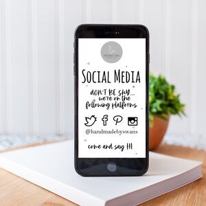 May include: A smartphone screen displaying social media icons for Twitter, Facebook, Pinterest, and Instagram. The text on the screen reads "SOCIAL MEDIA don't be shy... we're on the following platforms @handmadebyswans come and say HI".
