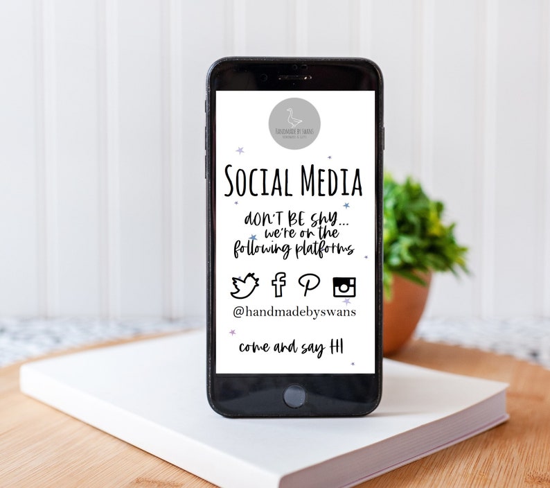 May include: A smartphone screen displaying social media icons for Twitter, Facebook, Pinterest, and Instagram. The text on the screen reads "SOCIAL MEDIA don't be shy... we're on the following platforms @handmadebyswans come and say HI".