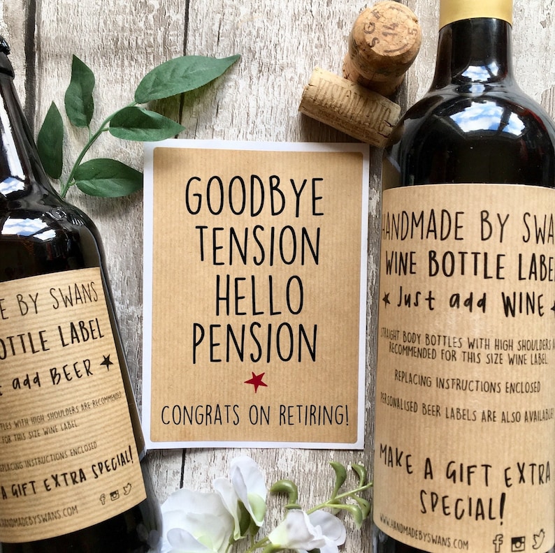 Puede incluir: Dos botellas de vidrio oscuro con etiquetas de papel color canela y texto en negro, incluyendo "HANDMADE BY SWANS" y "Just add WINE" o "Just add BEER". Una tarjeta rectangular central dice "GOODBYE TENSION HELLO PENSION CONGRATS ON RETIRING!" con una peque&ntilde;a estrella roja.