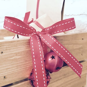 Puede incluir: Una caja de madera de color marr&oacute;n claro que contiene un regalo envuelto en papel beige liso. Una cinta de grosgrain roja con bordes cosidos en blanco est&aacute; atada en un lazo alrededor del paquete, con dos cascabeles rojos met&aacute;licos.