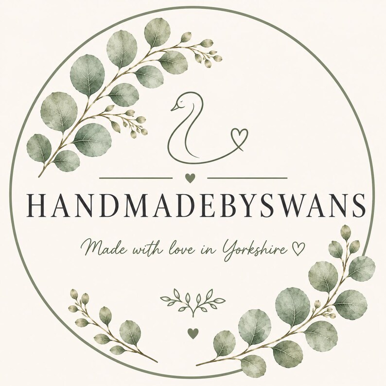 Puede incluir: Un logotipo circular que presenta el contorno estilizado de un cisne y ramas de eucalipto verdes. El texto dice HANDMADEBYSWANS y Made with love in Yorkshire, acompa&ntilde;ado de peque&ntilde;os iconos de corazones y un elemento decorativo de hoja.