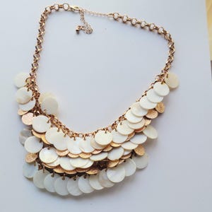 May include: A white ceramic mug with a black handle and the text "But First, Coffee" in a bold, black font. The mug is set against a blurred background, suggesting a cozy setting.